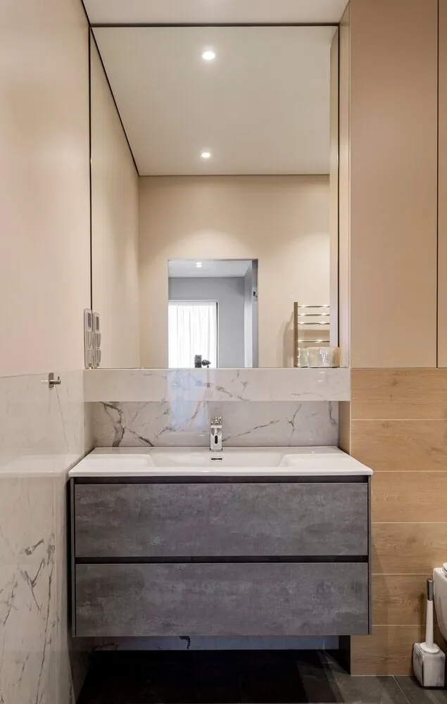 Al lado del lavabo siempre falta espacio, siempre es poco. Por lo tanto se implementó una solución con un estante de construcción, que es invisible y funcional. Encima del inodoro se colocó un armario espacioso para todo lo necesario en el baño. El armario fue hecho a medida.