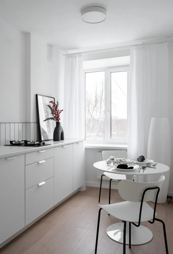 En la cocina se eligió una mesa blanca circular con diámetro de 80 cm, complementada por dos sillas con formas interesantes y manteniendo la paleta de colores blanco-negro del espacio.