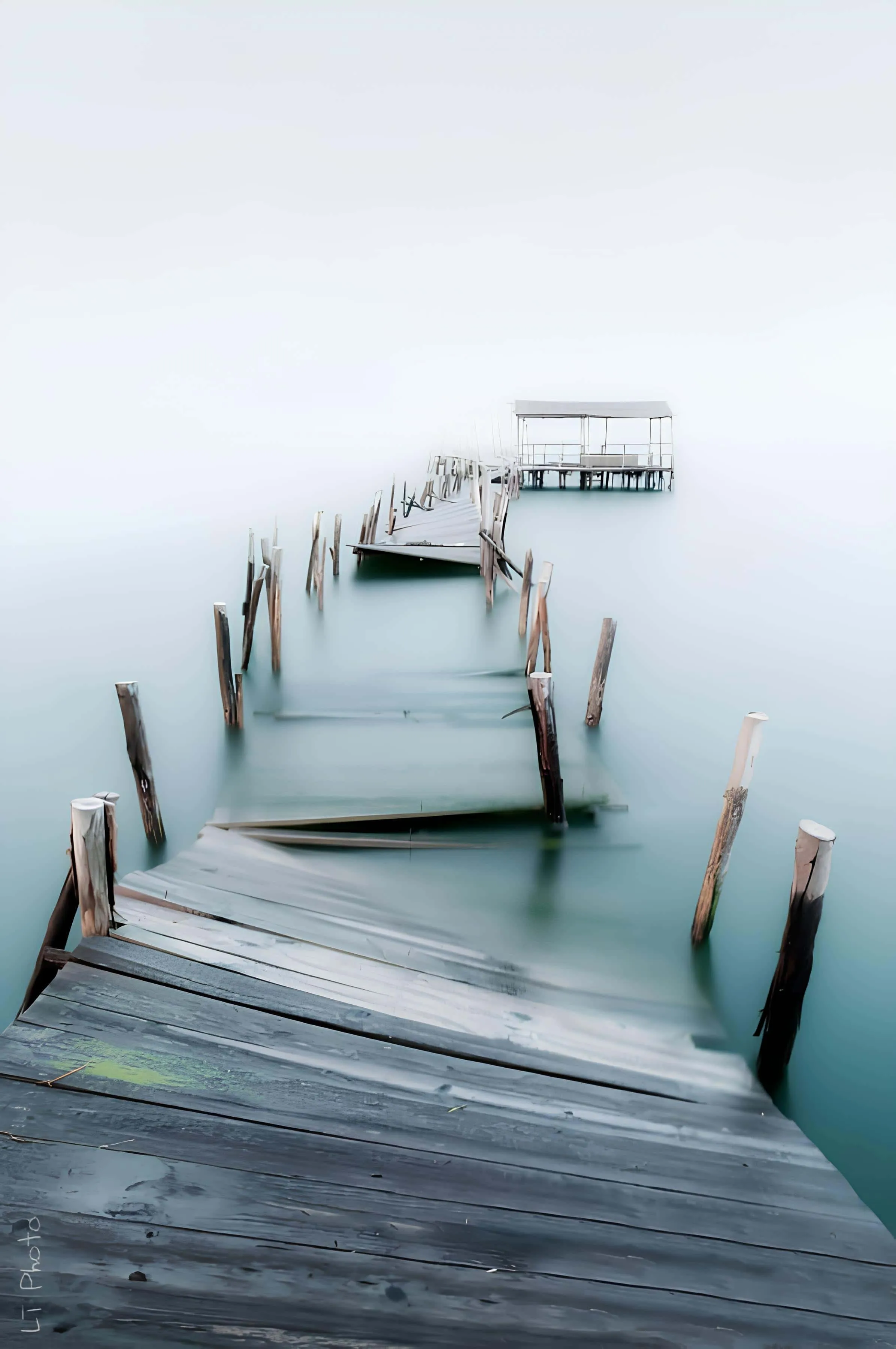 Decaying wooden dock sinking into fog over calm water