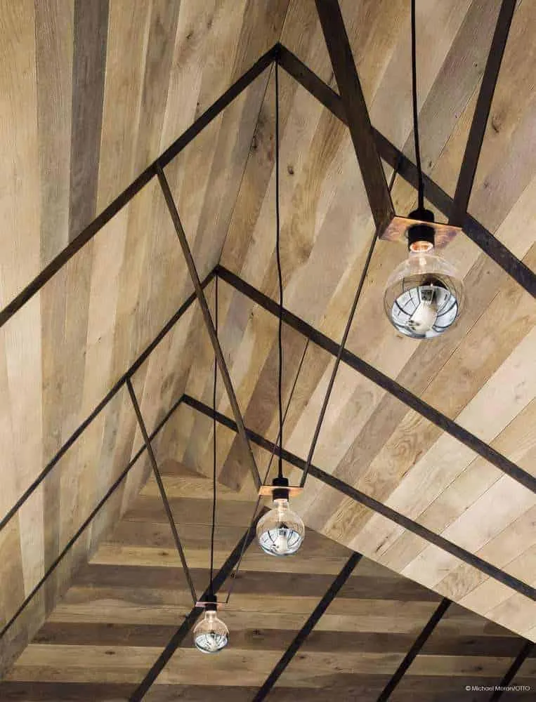Vista detallada de un techo de madera angular con lámparas colgantes minimalistas.