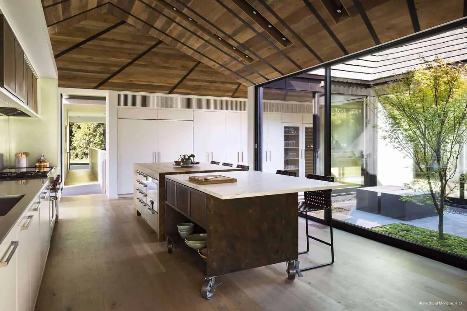 Large kitchen island next to glass walls opening onto green courtyard.