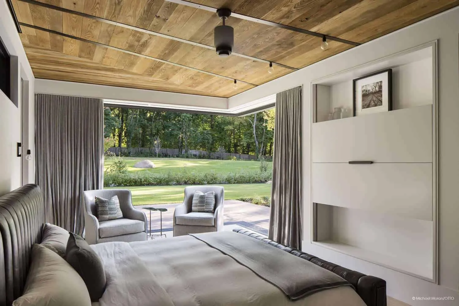 Cozy bedroom with view to garden through floor-to-ceiling windows.