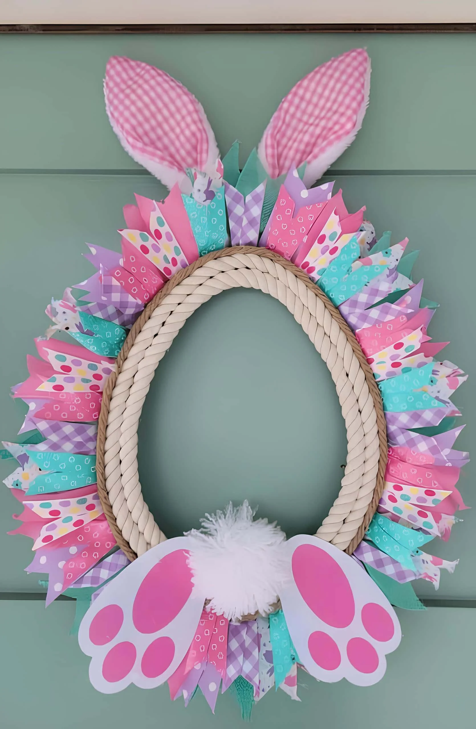 DIY guirnalda de Easter con conejo, hecha con marco ovalado envuelto en cuerda, cinta pastel, orejas de conejo en gamuza rosa, cola blanca de peluche y patas rosadas del conejo - decoración festiva brillante para puerta primaveral