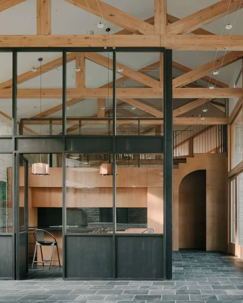 Angled view from outside: mass of stone, wooden cornices and sky reflection in glass.