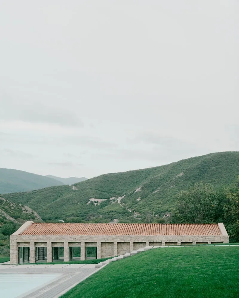 Georgian house in Tvaladi with stone walls and wooden volumes against the backdrop of hills.