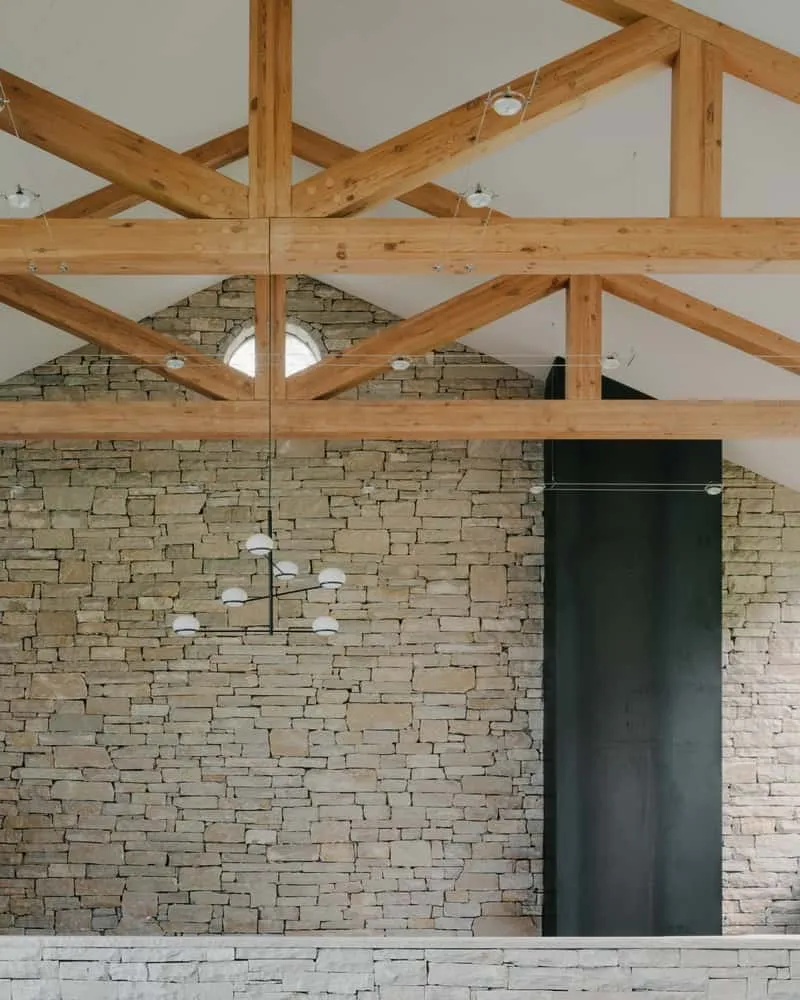 Living room with wooden ceiling, stone accent wall and panoramic stained glass windows towards the landscape.