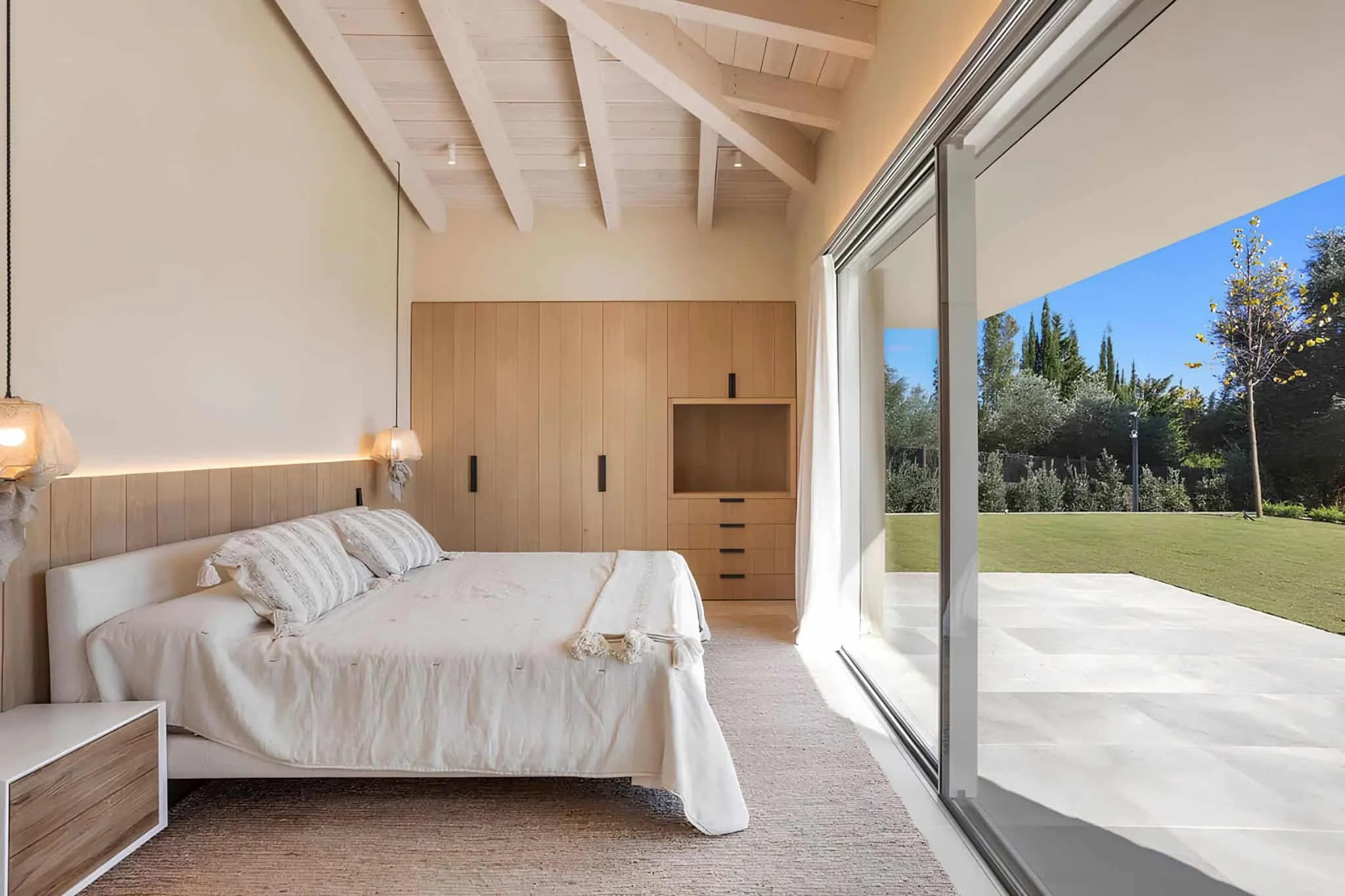 Dormitorio mediterráneo minimalista con acentos de madera y puertas de vidrio completas.