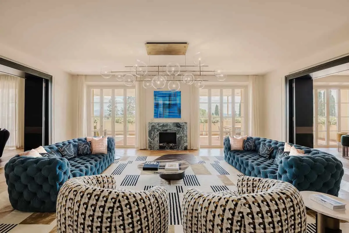 Luxurious living room with modern blue velvet sofas and contemporary design, large windows, marble fireplace and geometric rug for an elegant interior.