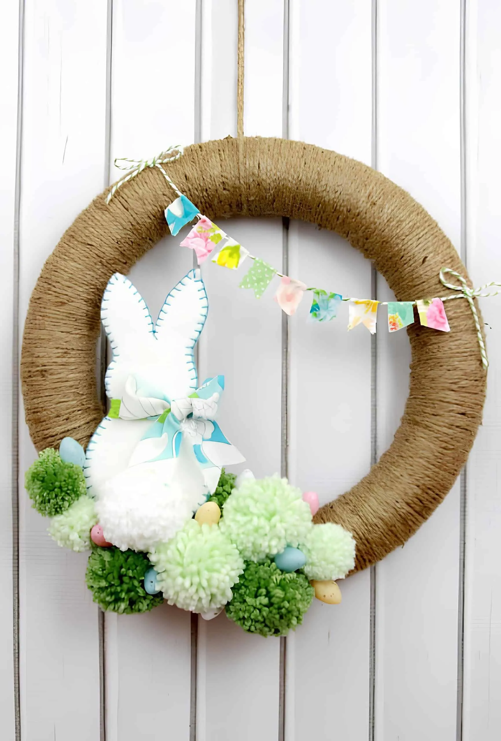 纱线门饰，配有毛绒兔子、粉彩兔耳朵、迷你鸡蛋和彩色旗帜，非常适合春季装饰。