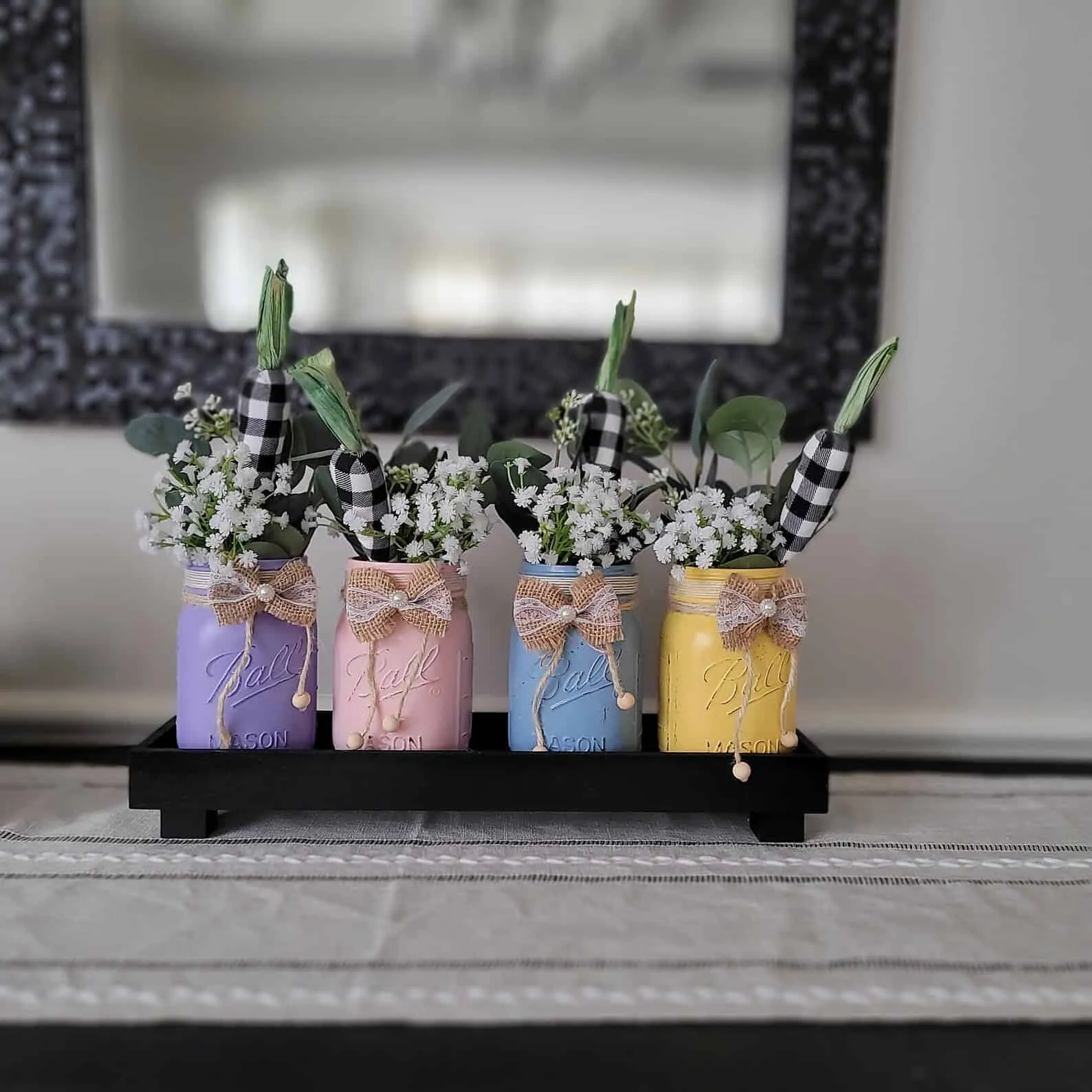 粉彩色复活节 Mason 罐子，装有人造花和胡萝卜装饰在黑色托盘上