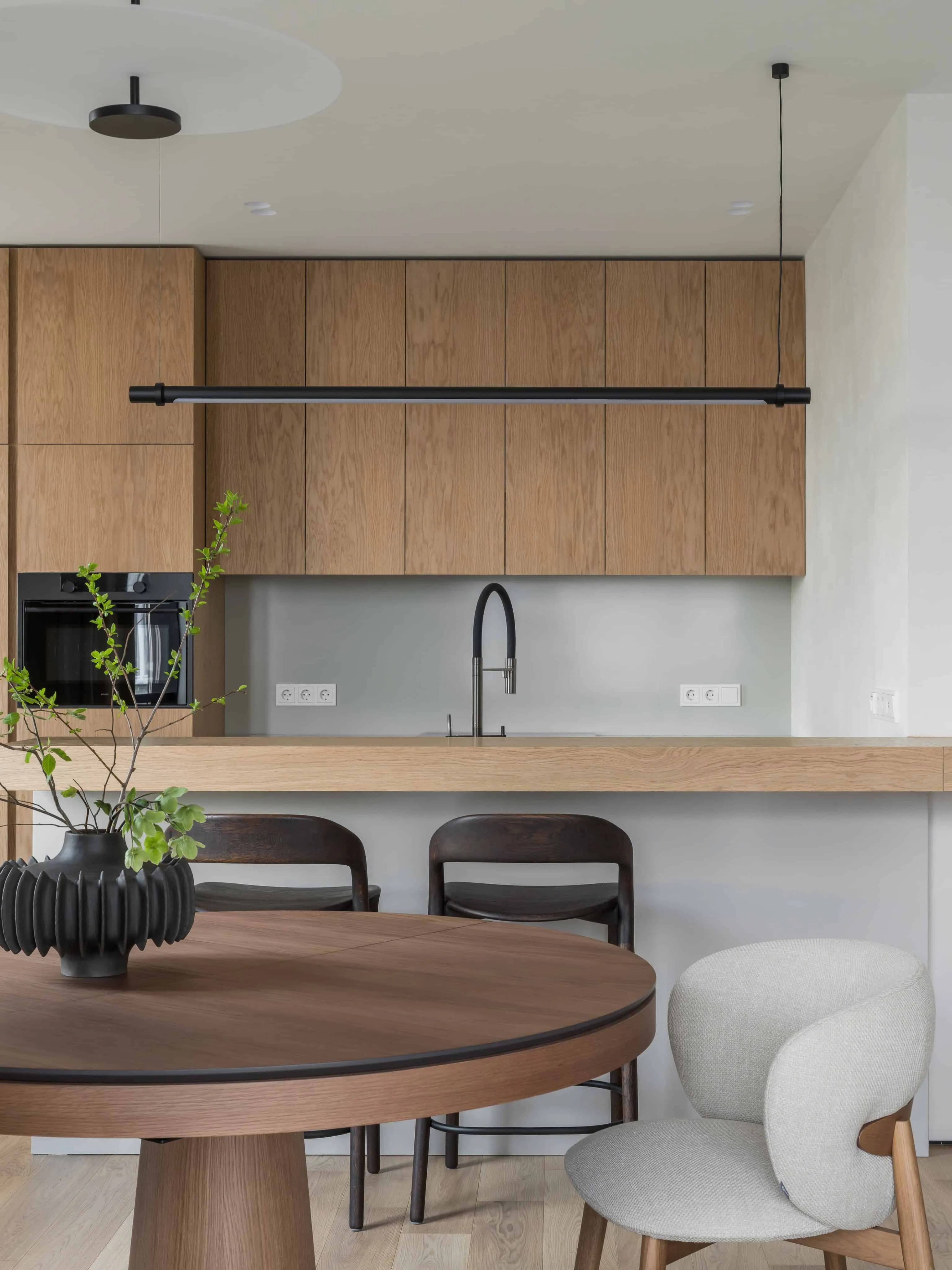 黑色固定装置的厨房岛台与木质椅子，在柔和极简主义室内环境中。