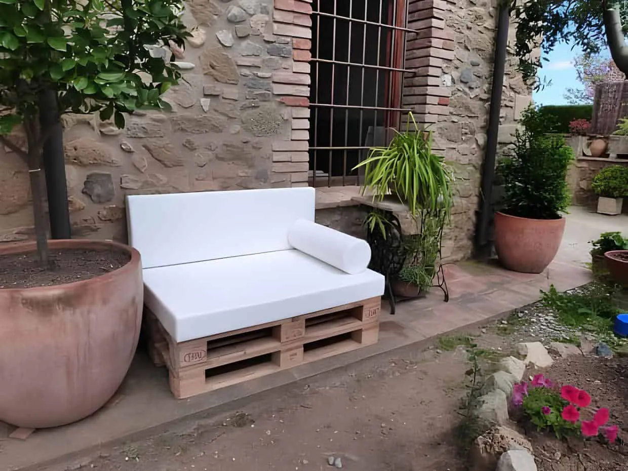 带有靠垫的白色托盘长椅，放置在石质庭院中