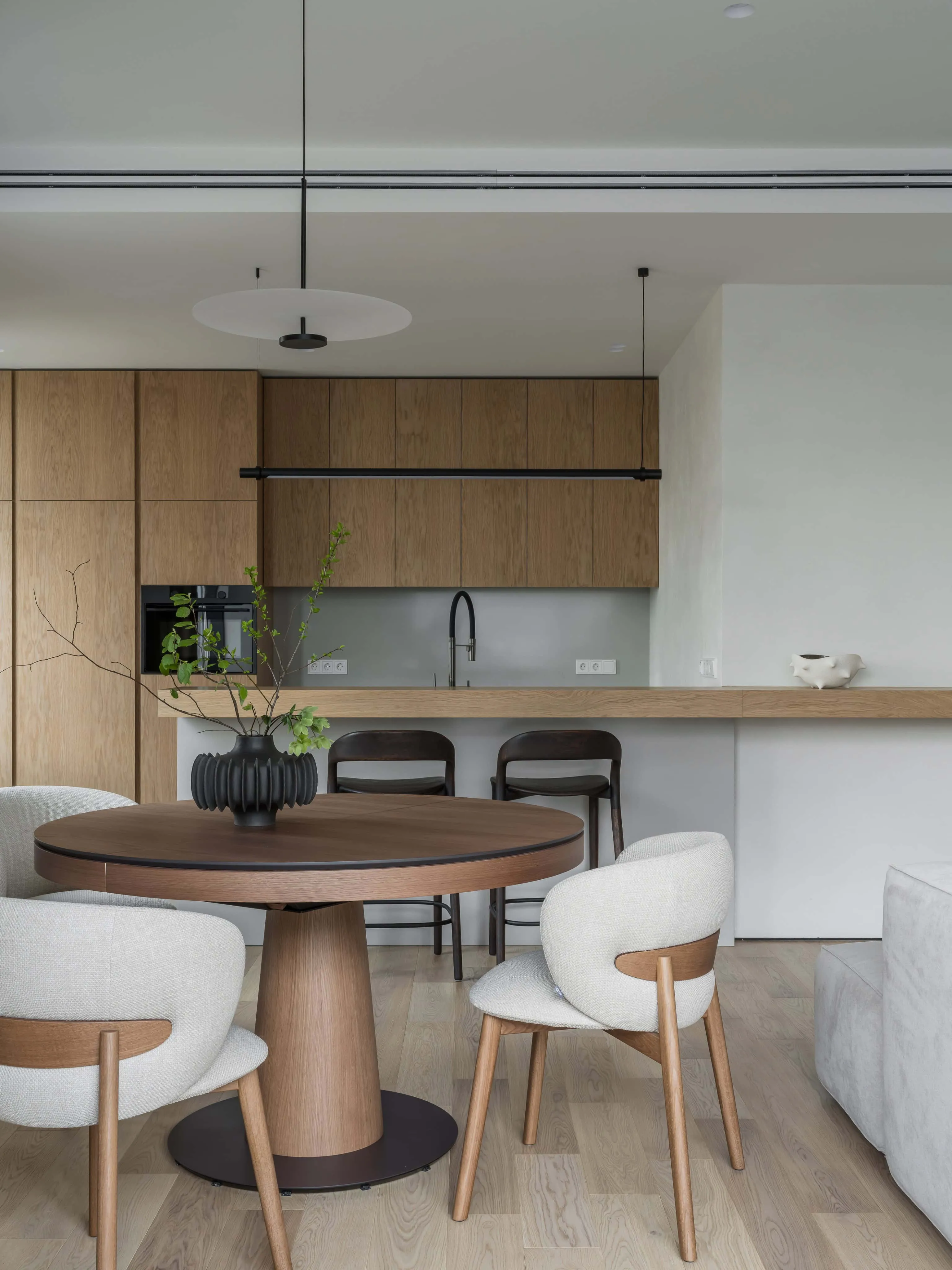 圆形木质餐桌与布艺椅子，现代厨房配自然光。