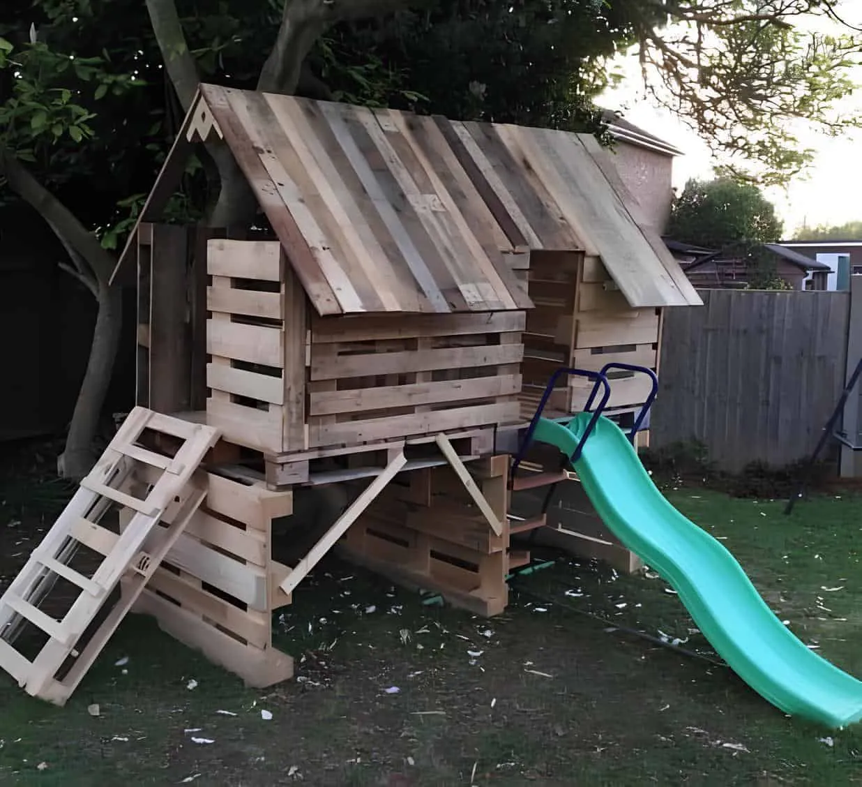 后院的双层木制托盘小屋，配有绿色塑料滑梯