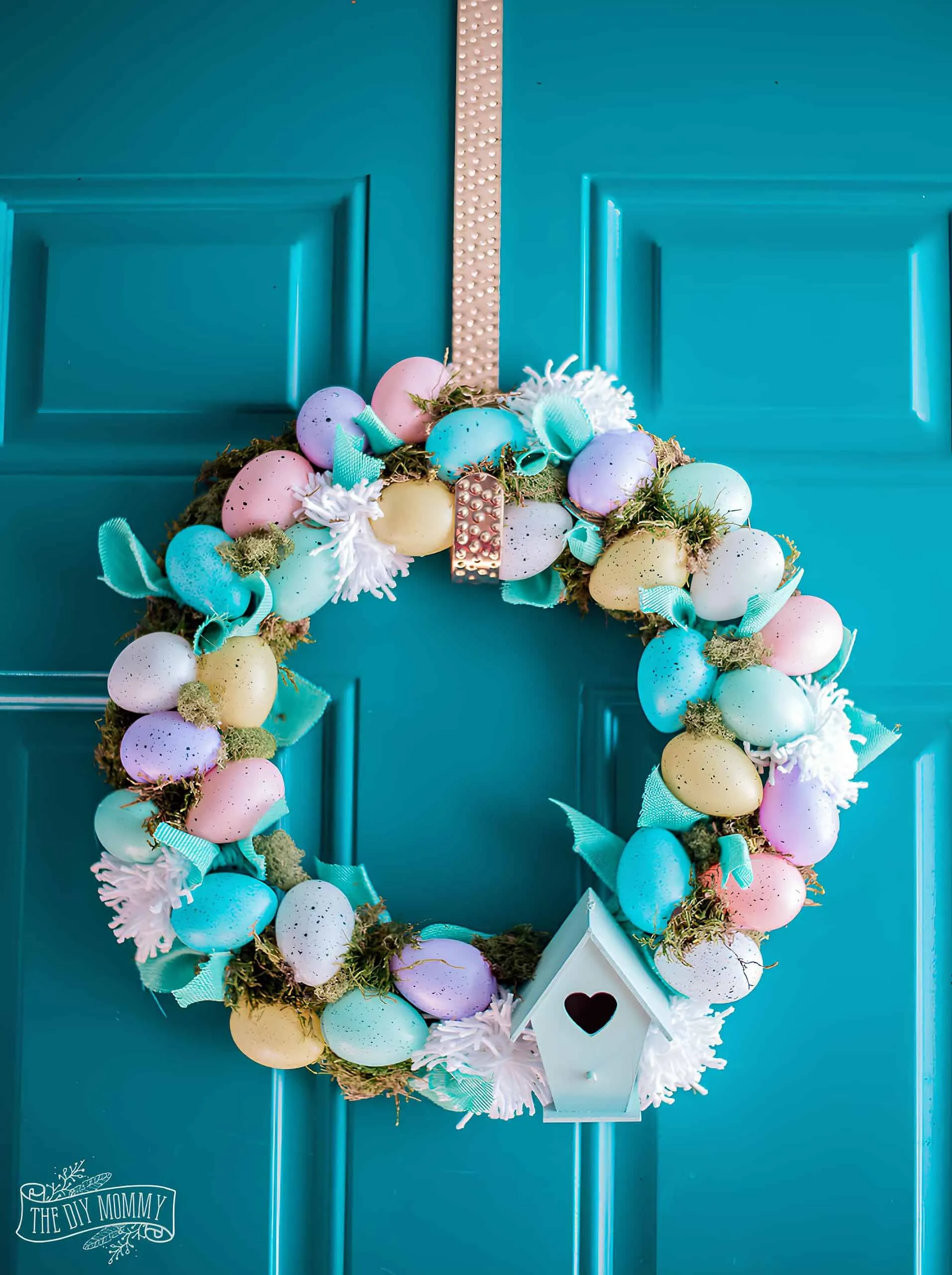 带有鸡蛋、苔藓、丝带和小鸟的花卉粉彩门饰，挂在蓝色门上——经济实惠的春季装饰。