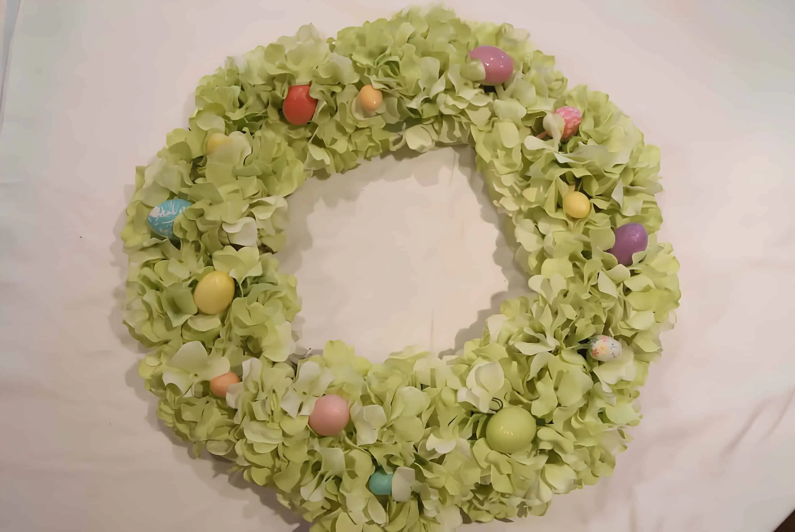 由假绿色花朵制成的门饰，配有粉彩直鸡蛋，散落在整个门饰上，在中性织物背景上。