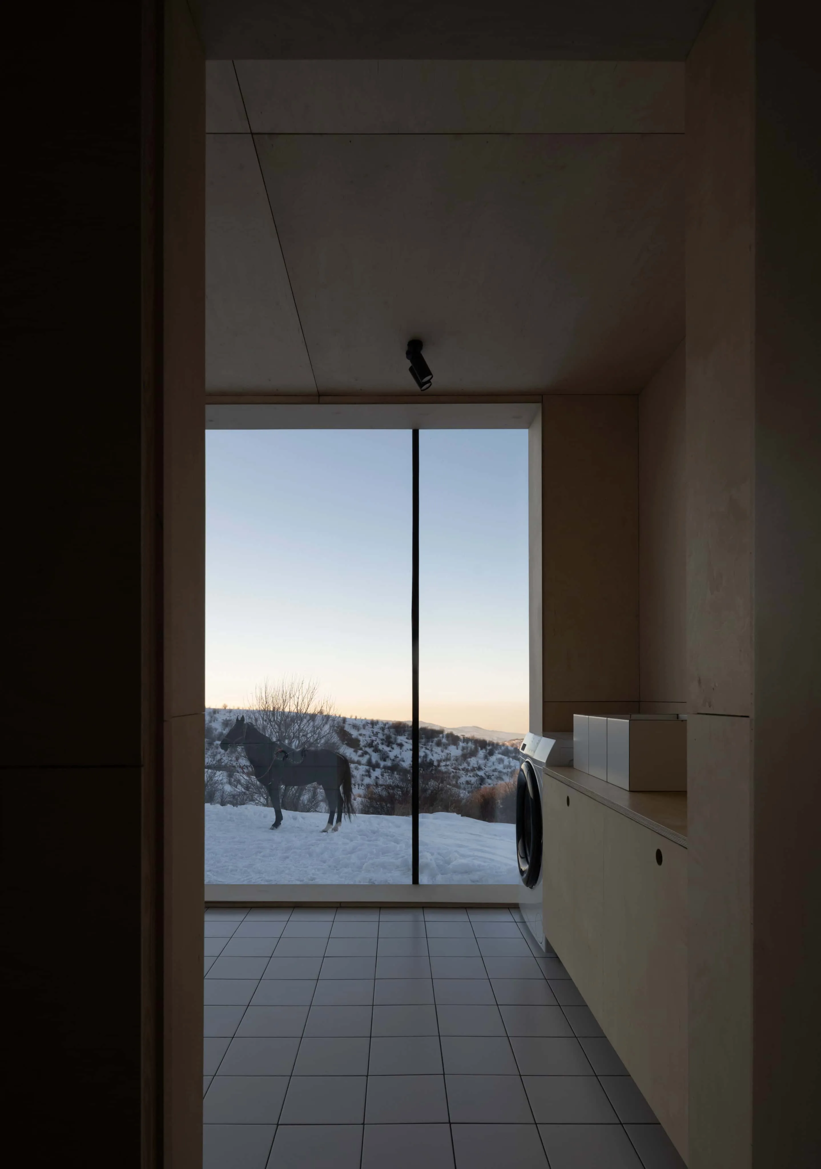 极简洗衣间，设有大窗直面雪地中的白马。