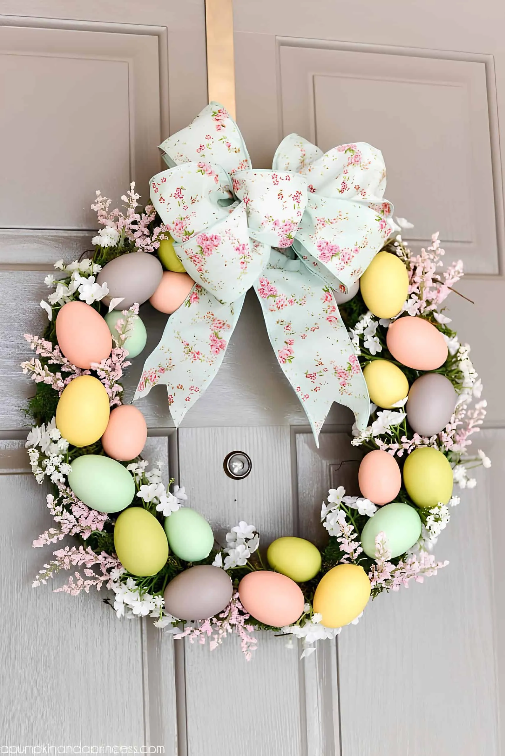 粉彩鸡蛋门饰，配有柔软的粉色和白色花朵及花丝带，挂在中性色门上。