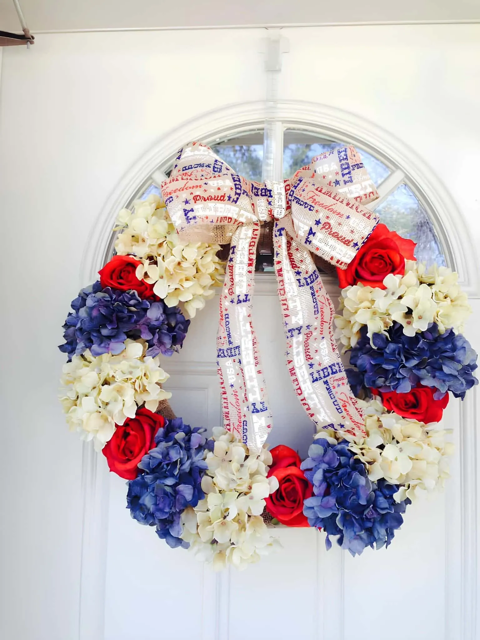 节日花环，配有蓝绣球花、红玫瑰和白花，带有爱国印花丝带