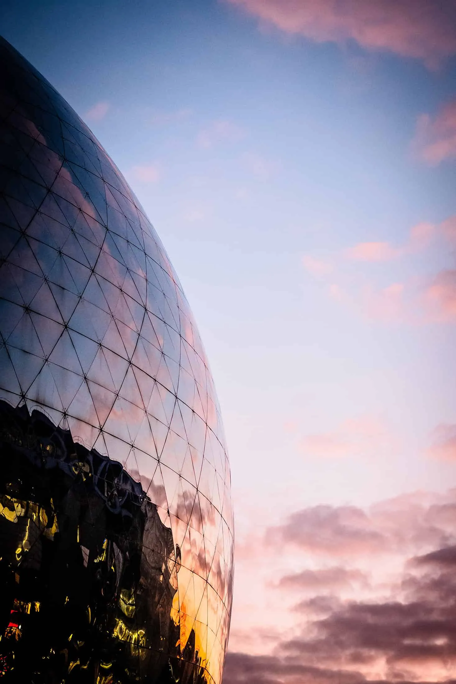 Detail of the reflective dome La Géode at sunset with bright clouds.