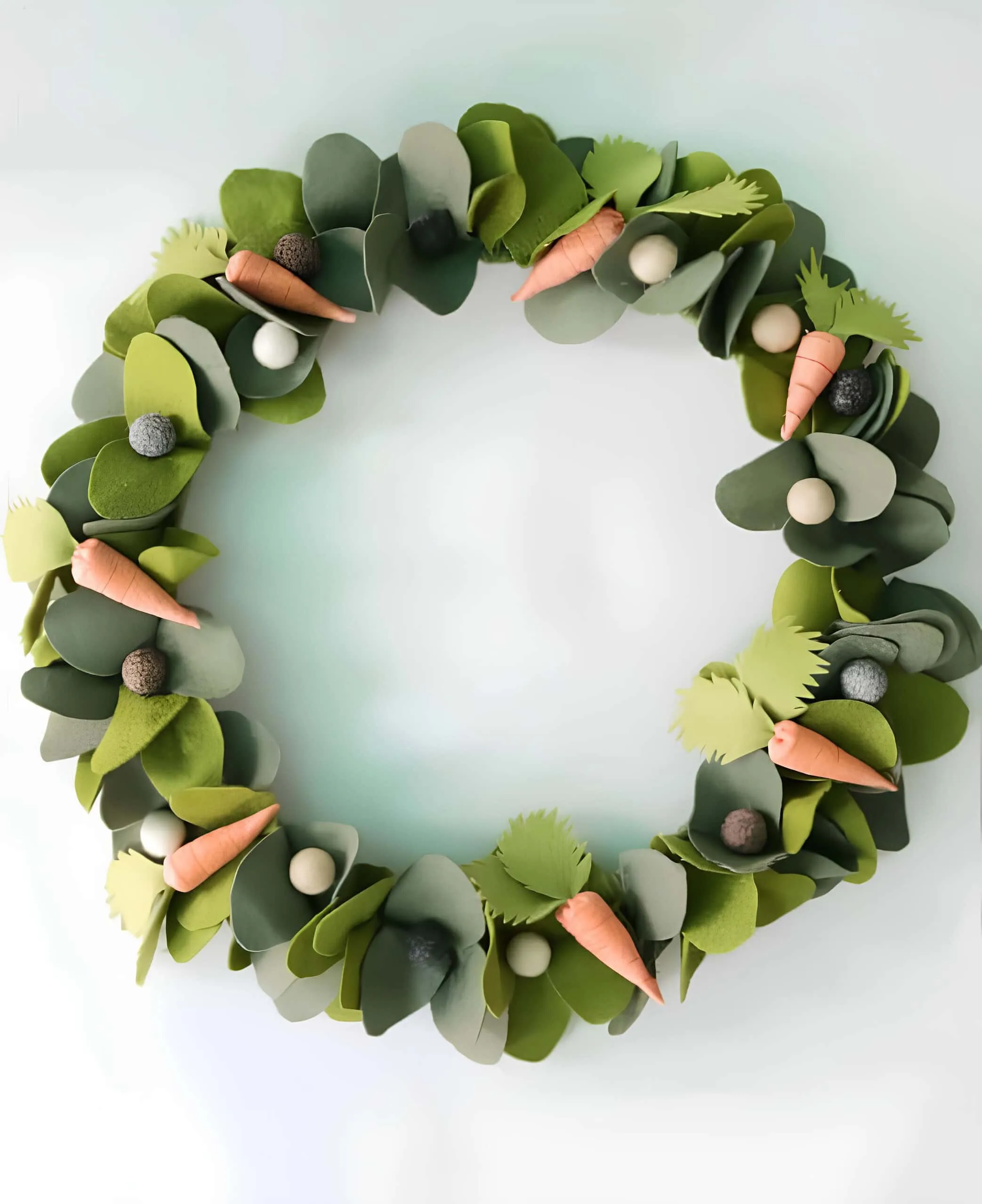 鸡蛋门饰，配有桉树叶层、柔软的毛毡球和迷你胡萝卜，呈现现代绿色风格。