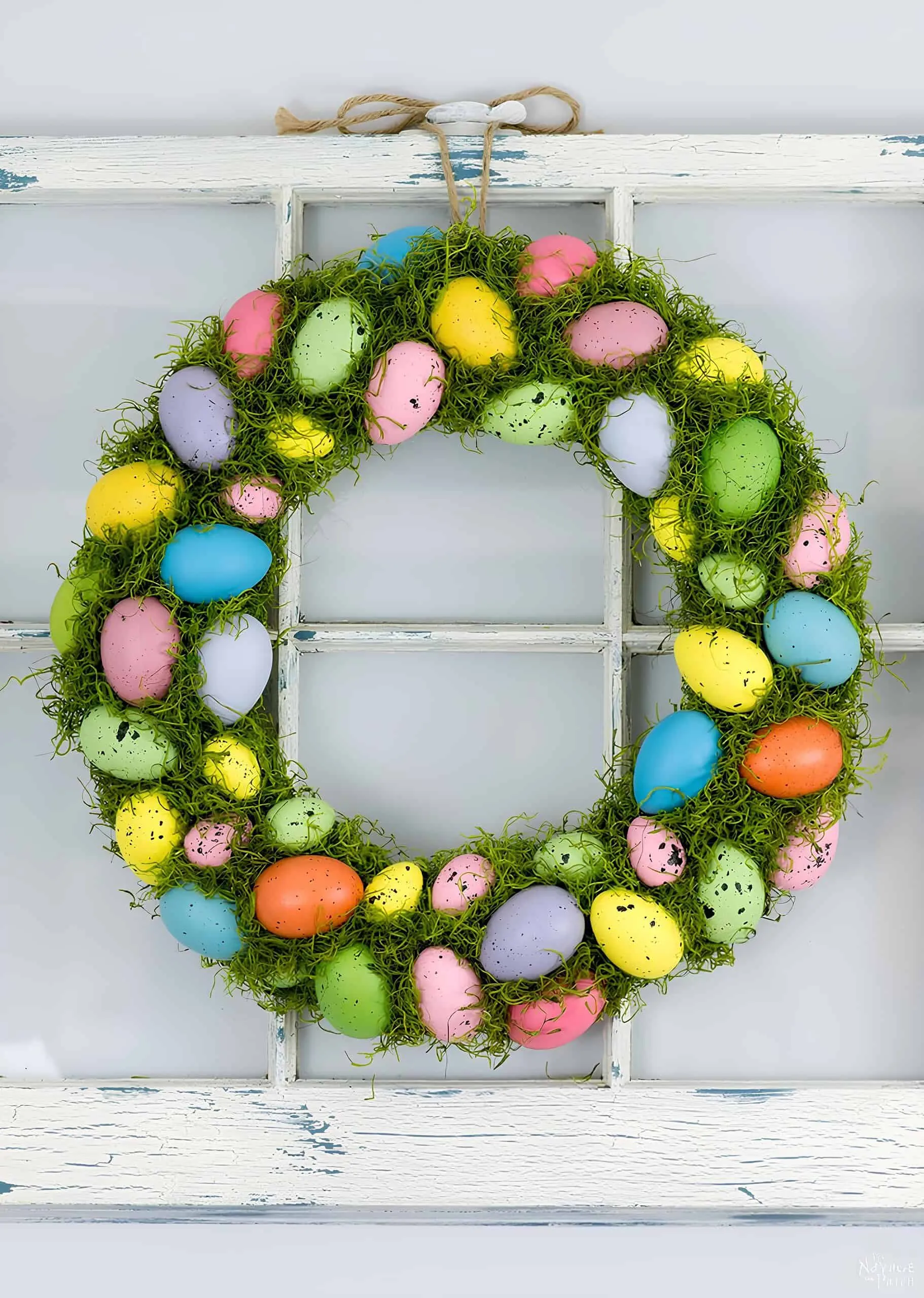 明亮且欢乐的鸡蛋门饰，用彩色花哨的鸡蛋和绿色苔藓悬挂在一个白色木框上。