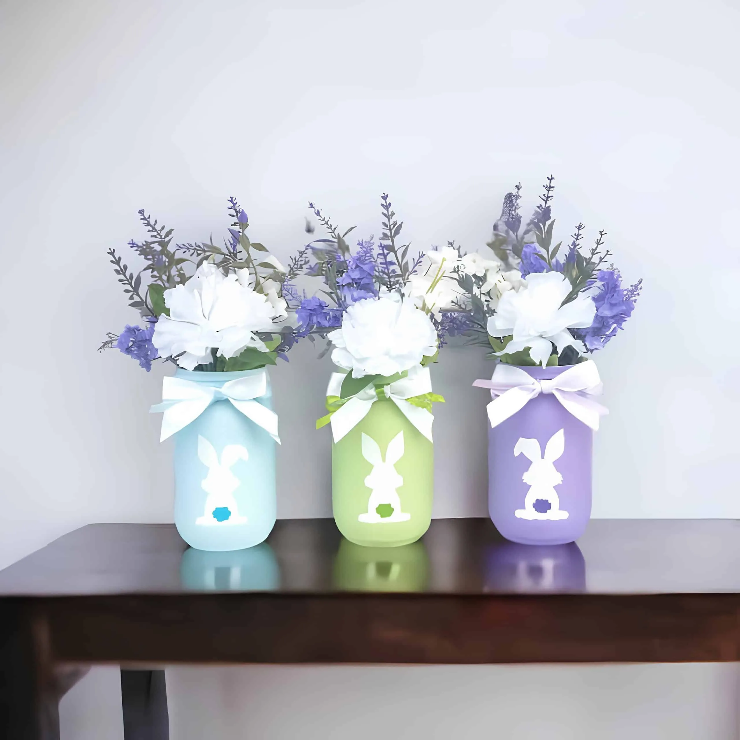 粉彩色 Mason 罐子，有白色兔子轮廓、丝带和白色与紫色复活节花