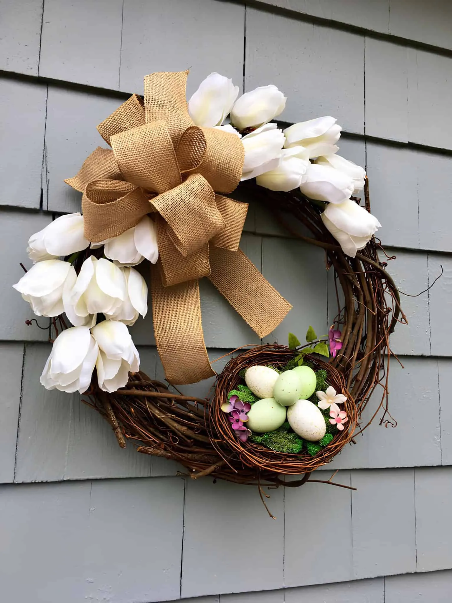 春天复活节门饰，配有白色郁金香、粗麻丝带和装有粉彩绿色鸡蛋的鸟巢