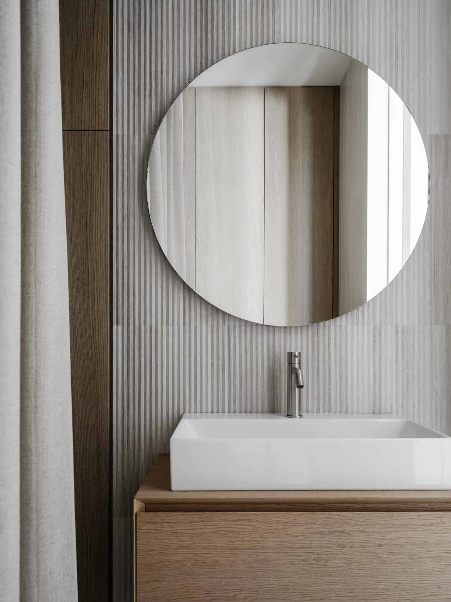 Round mirror frame above wooden sink in bathroom.