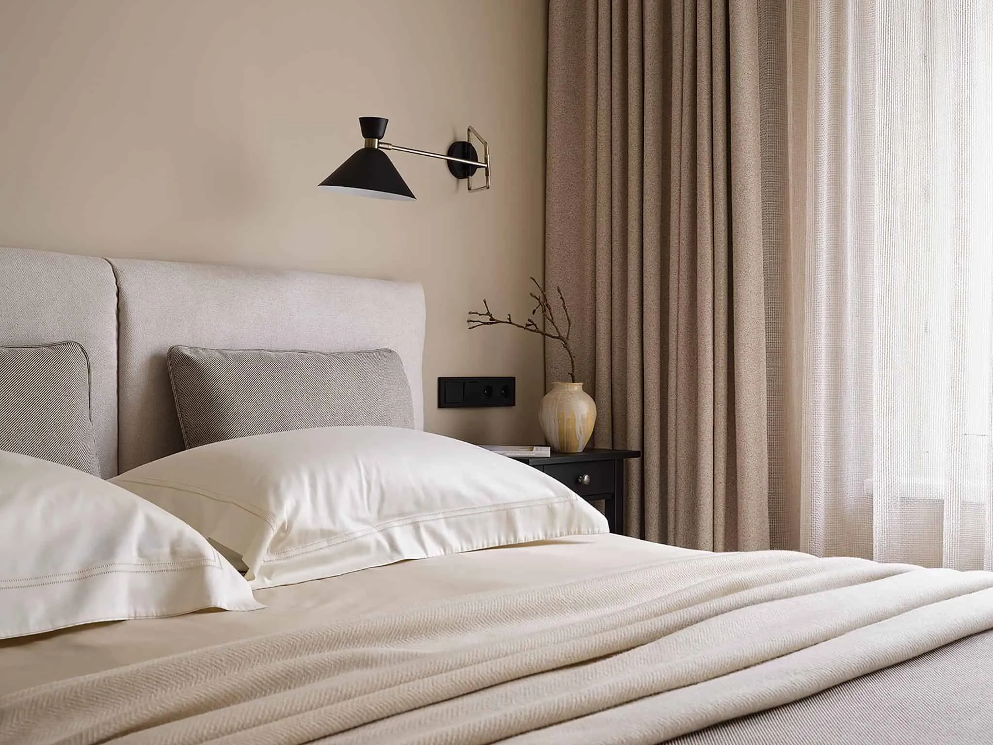 配有米色窗帘和柔和阳光透过半透明织物的卧室温馨角落。