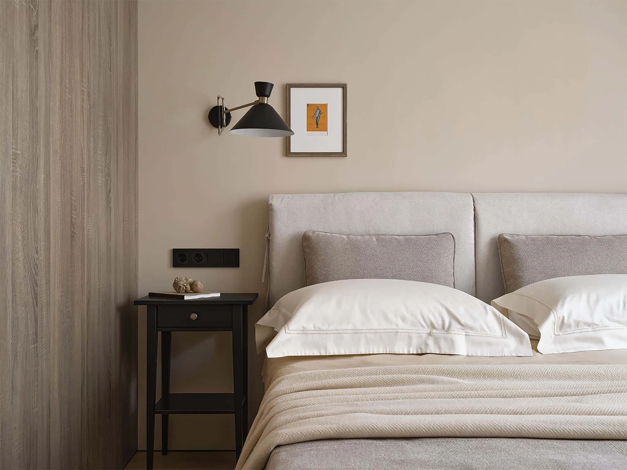中性卧室配有织物床头、黑色壁灯和床头柜上的画框。
