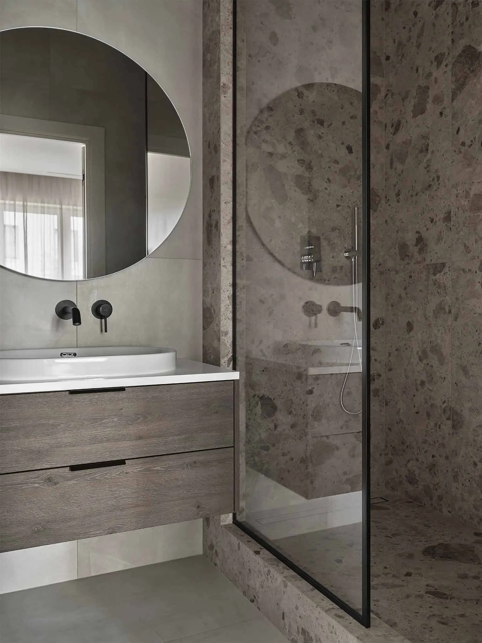 带有纹理石材墙面和带黑色固定件的木质洗手台的淋浴区。