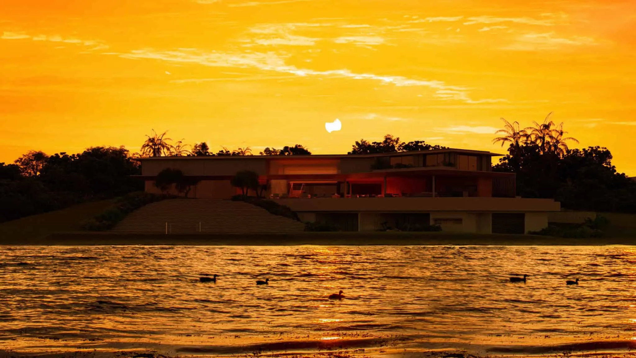 Silhouette of a lake-side villa under a bright orange sunset.