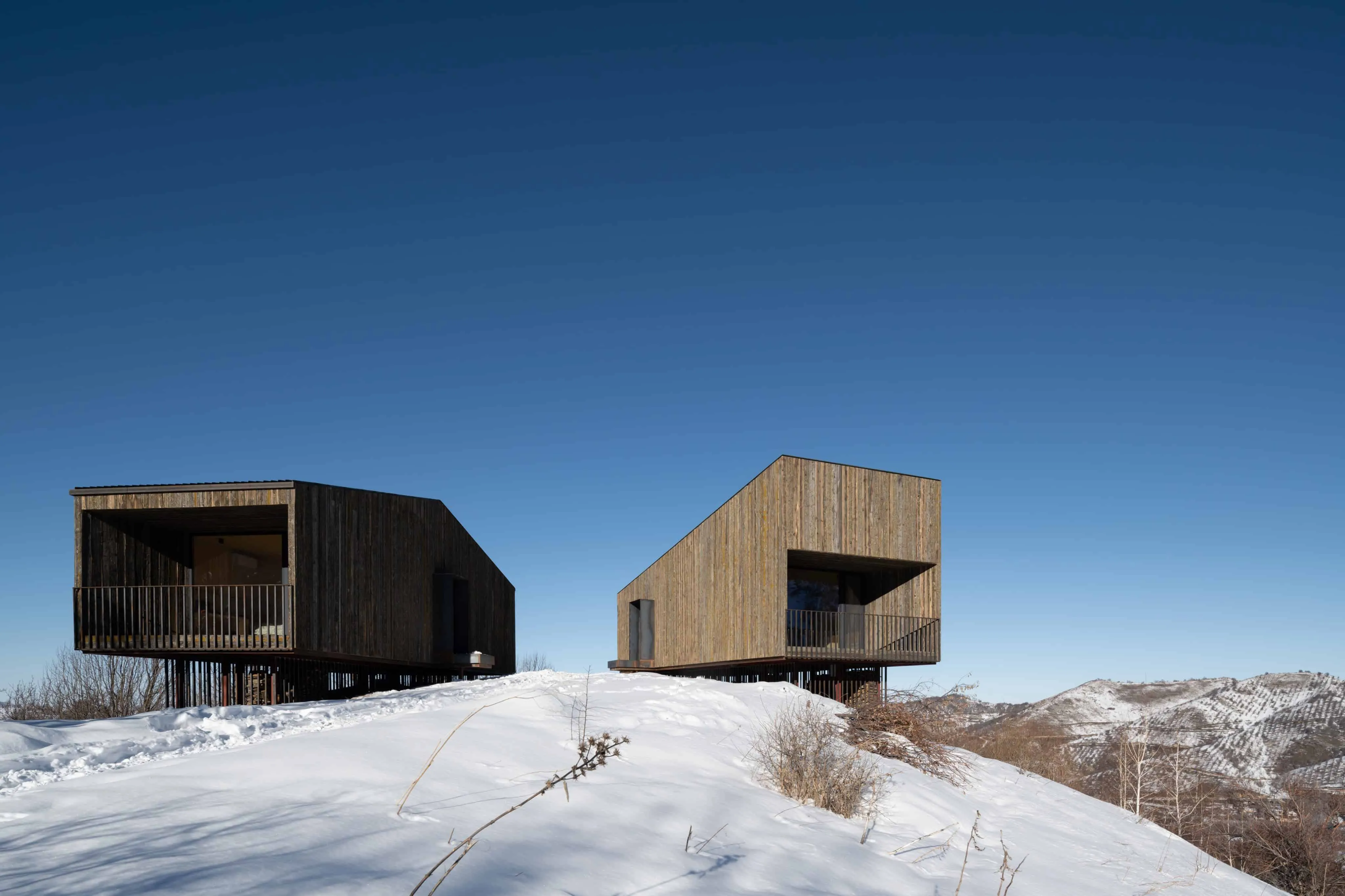 成对阿姆小屋矗立在雪峰上，晴朗蓝天之下。