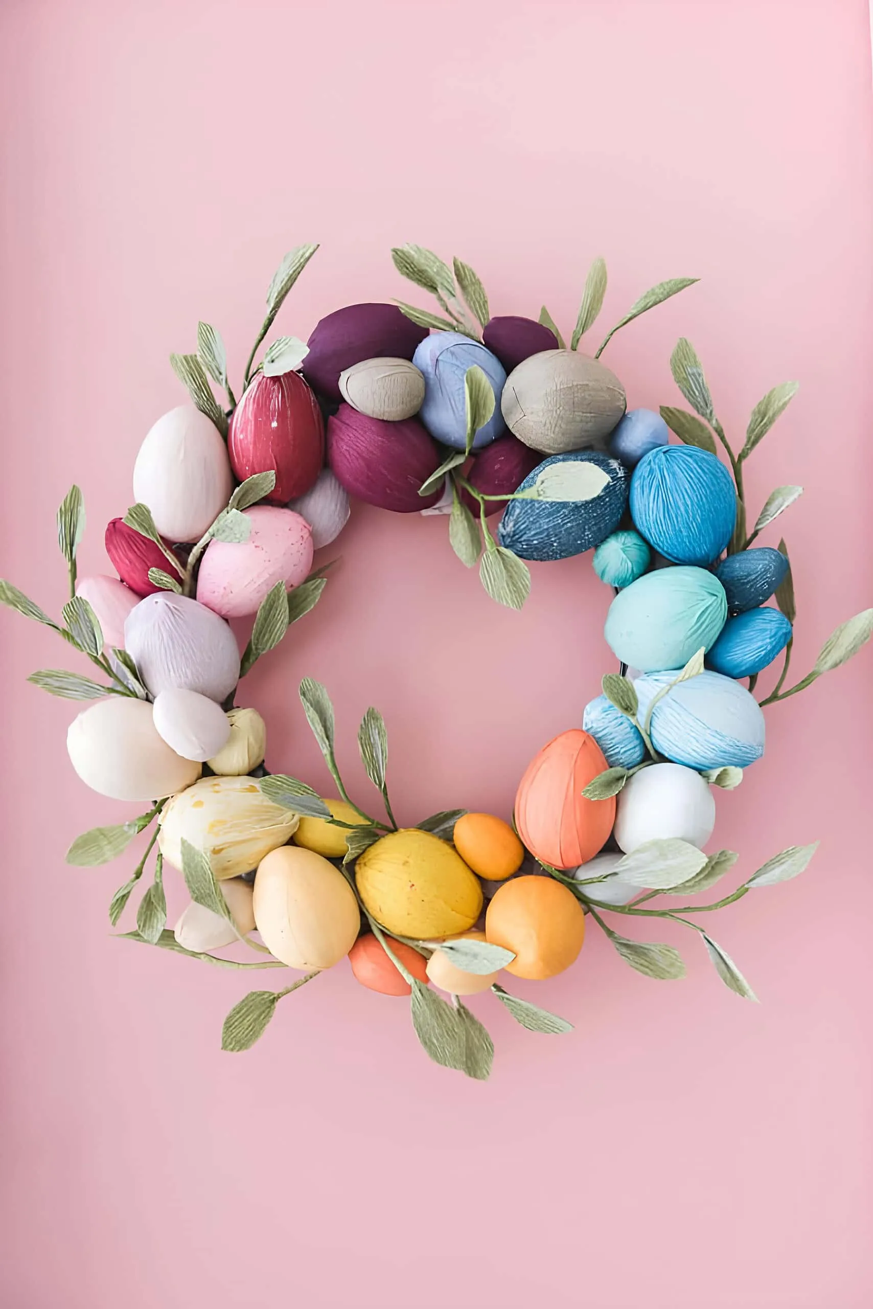 现代鸡蛋门饰，手工染色成彩虹色和细绿色叶子，在粉色背景上。