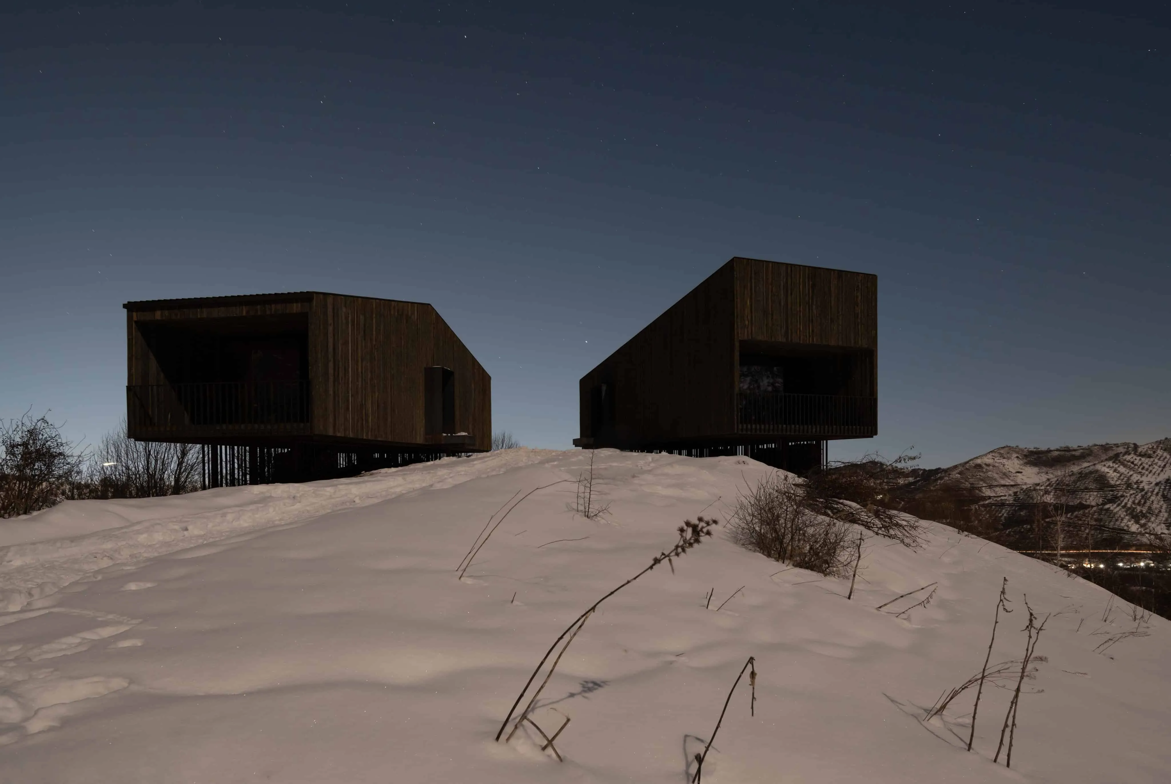 两间阿姆小屋矗立在雪坡上，星空之下。