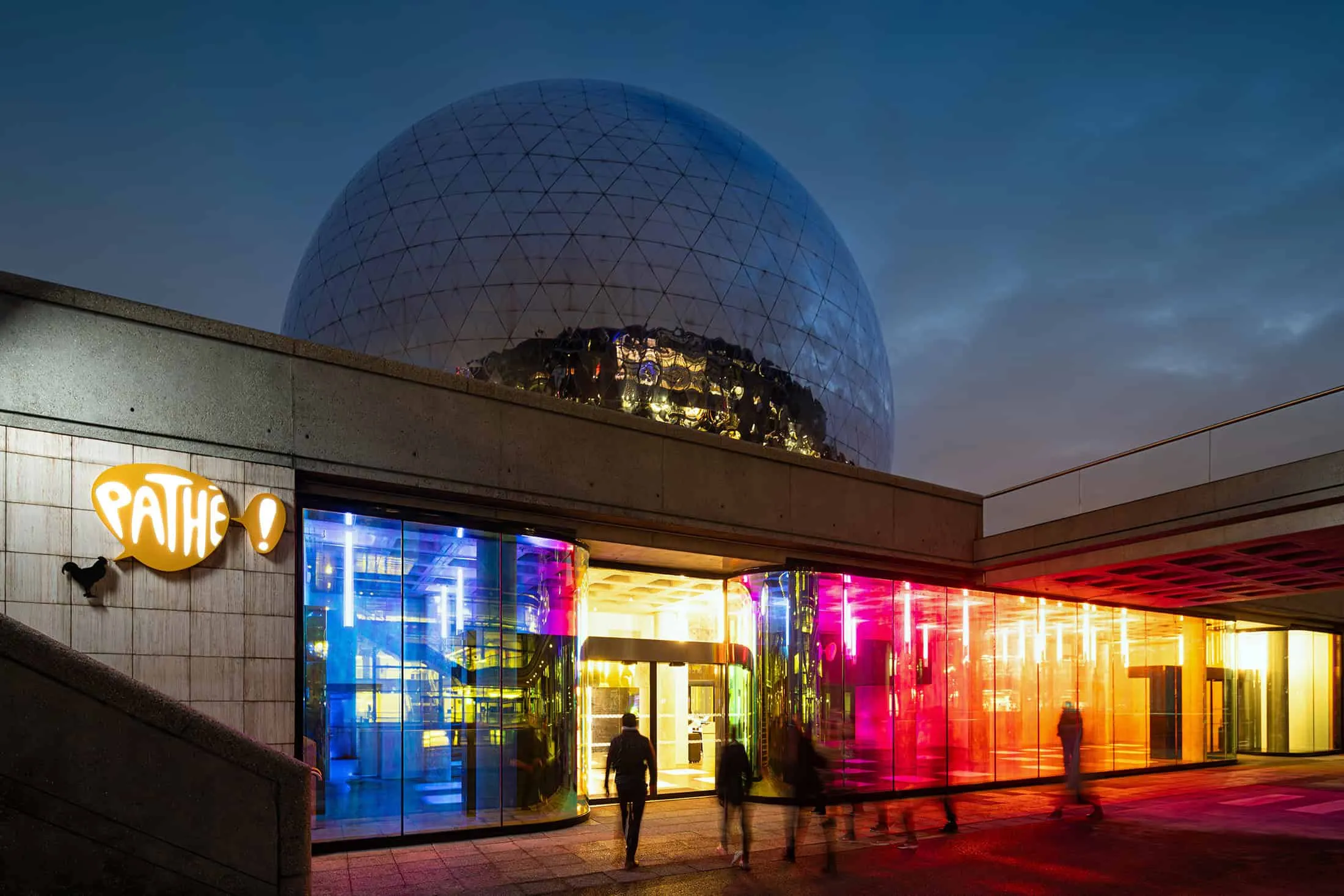 Exterior view of La Géode with a colorful glass facade structure illuminated at night.