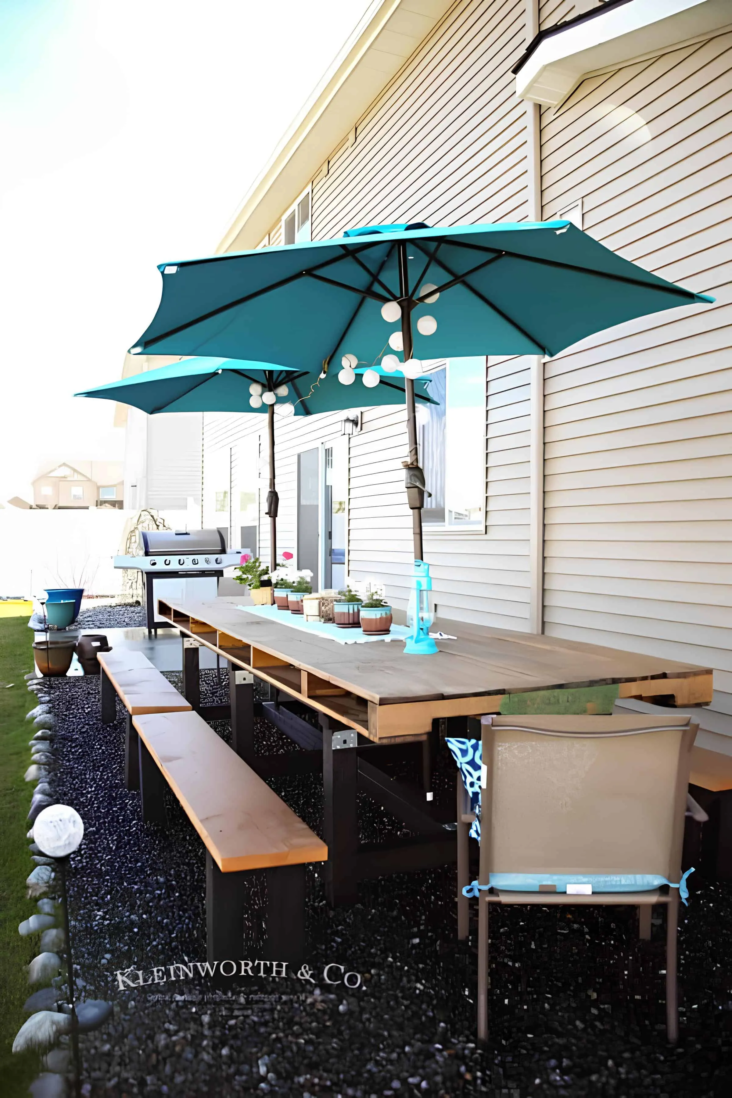 由托盘制成的大餐桌，配有长长的长凳和遮阳伞，在碎石露台上