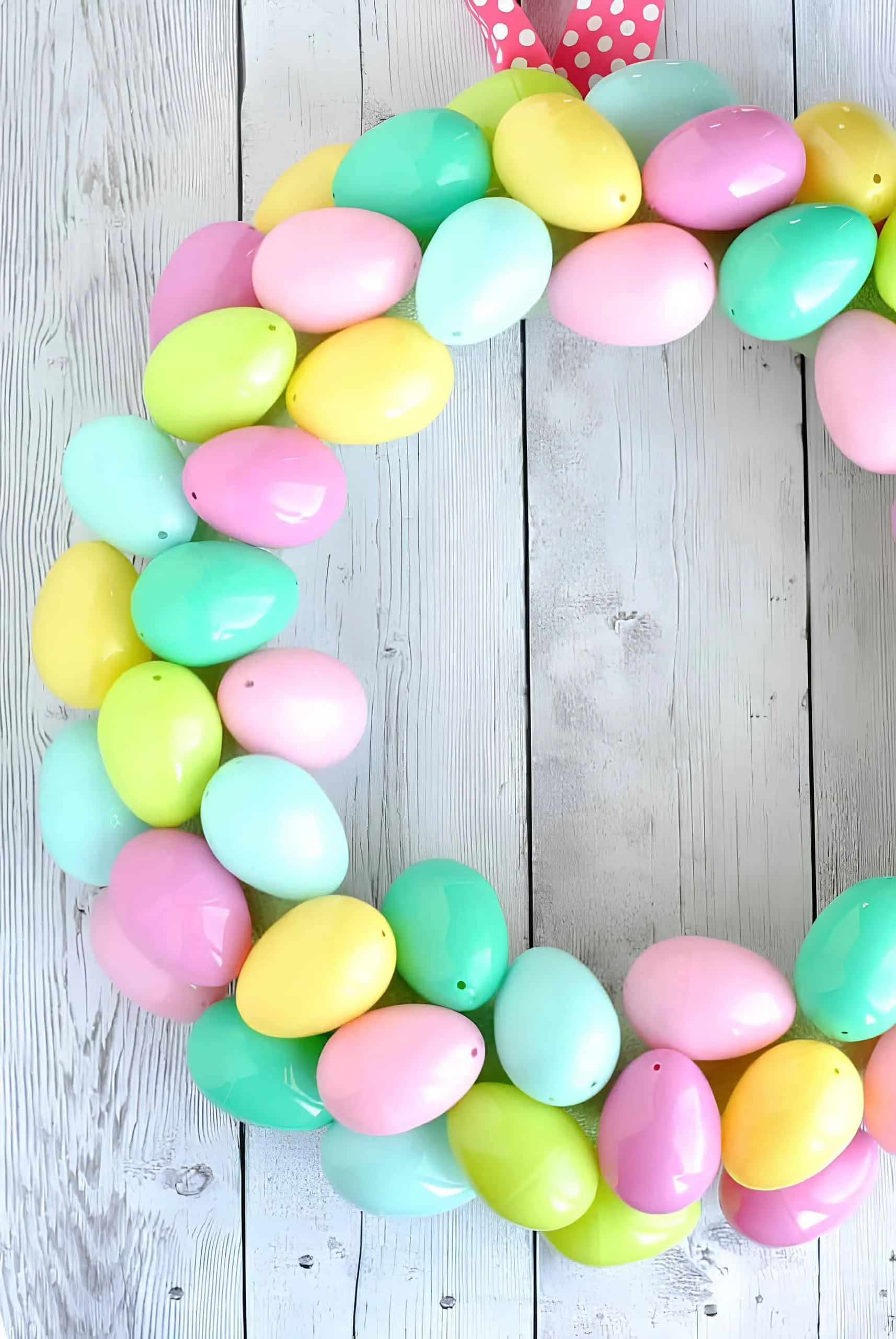 手工制作的粉彩塑料鸡蛋门饰，柔和的粉色、黄色、绿色和蓝色，悬挂在白色木头上配粉色条纹丝带。