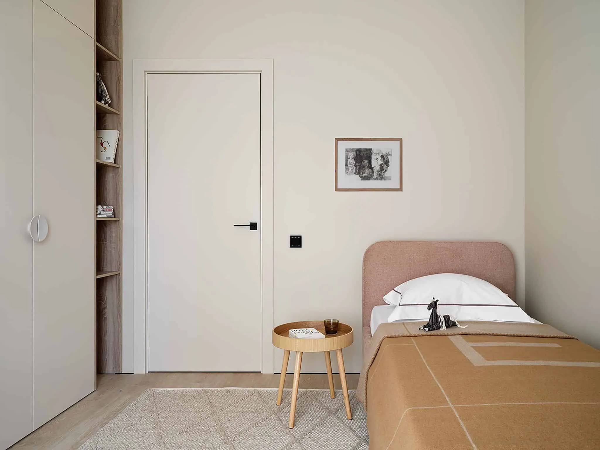 米色配色的极简儿童房，配有柔软床头和内置书架。