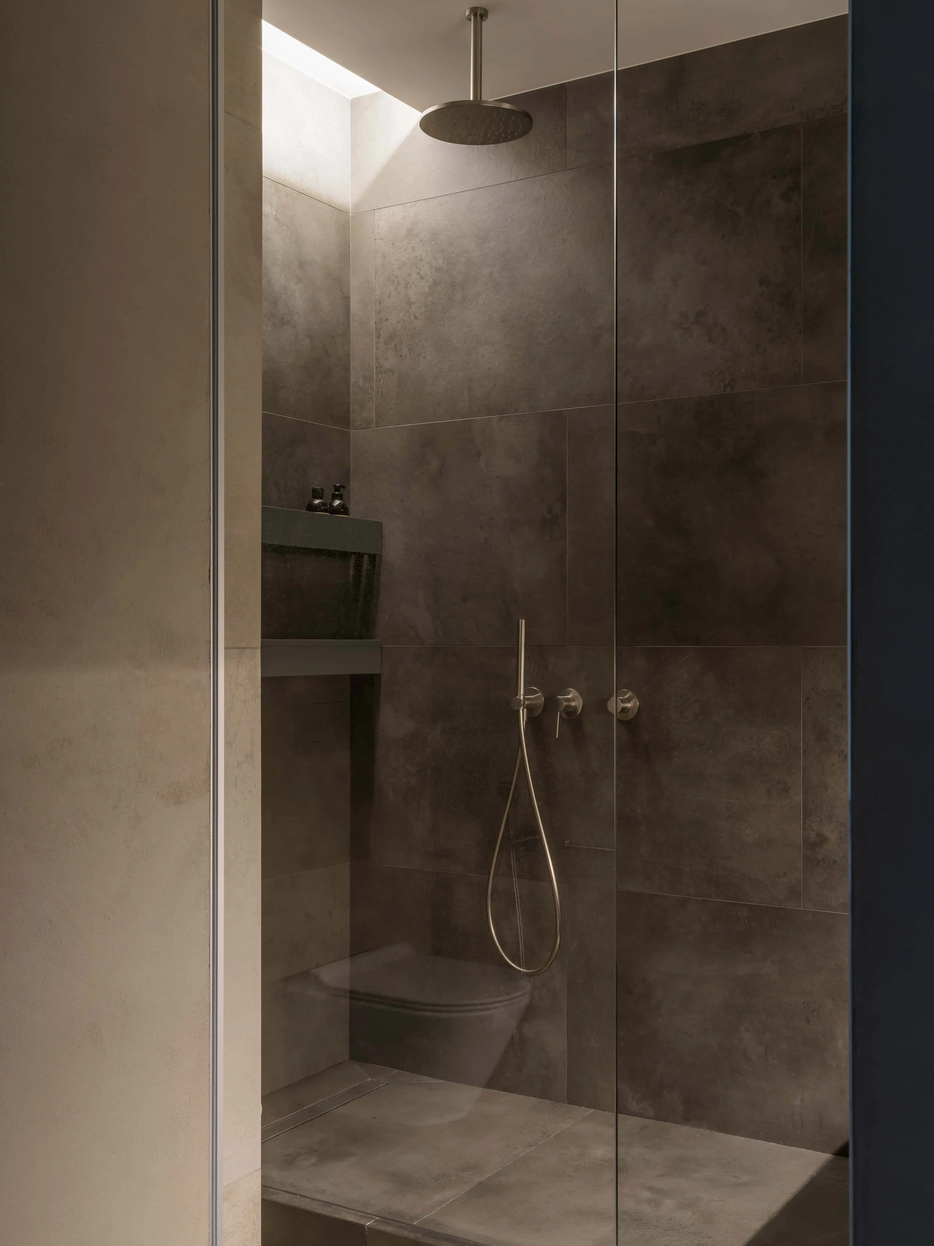 极简淋浴角落，配有通道玻璃淋浴和雨喷头。