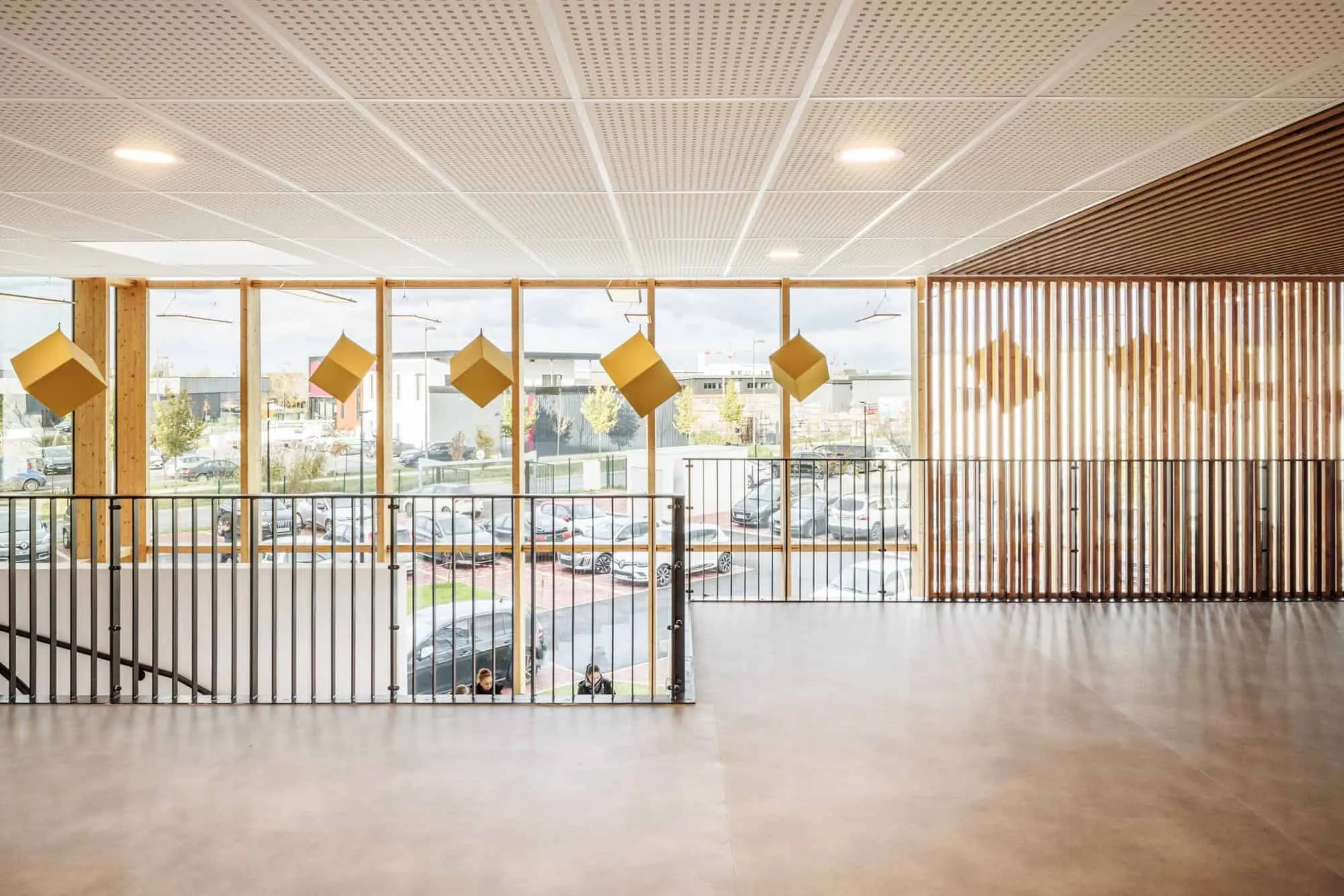 Upper level hall of the Mennese Sports Complex with playful cubic pendant lights and wooden partitions.