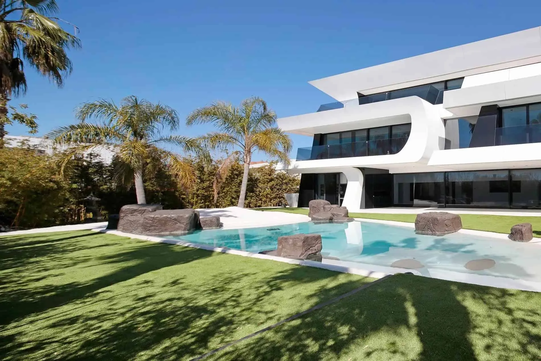 现代白色别墅侧面视图，带有弯曲线条和游泳池边热带花园