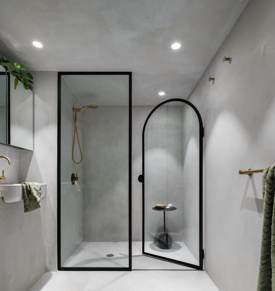 Brutal bathroom with arched glass shower and minimalist gold accents