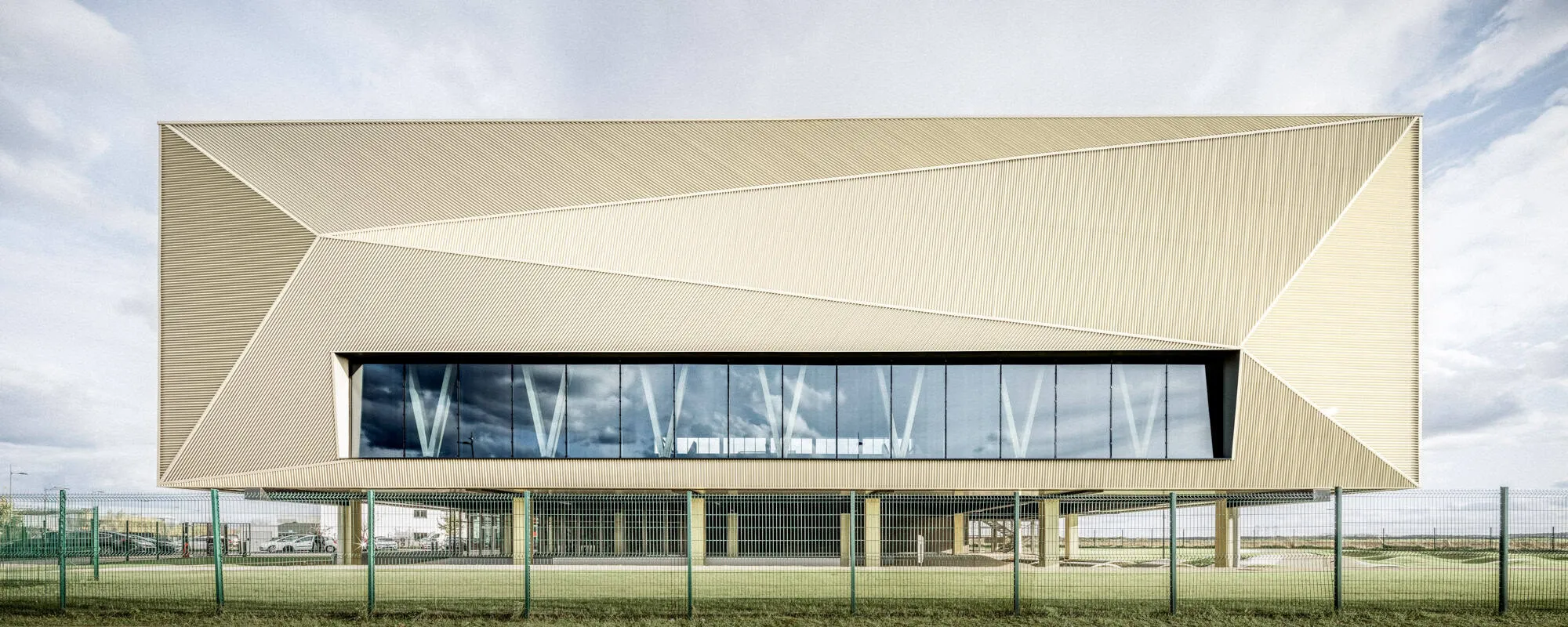 Main facade of the Mennese Sports Complex, designed by Atelier Aconcept, showing bold geometric cladding.