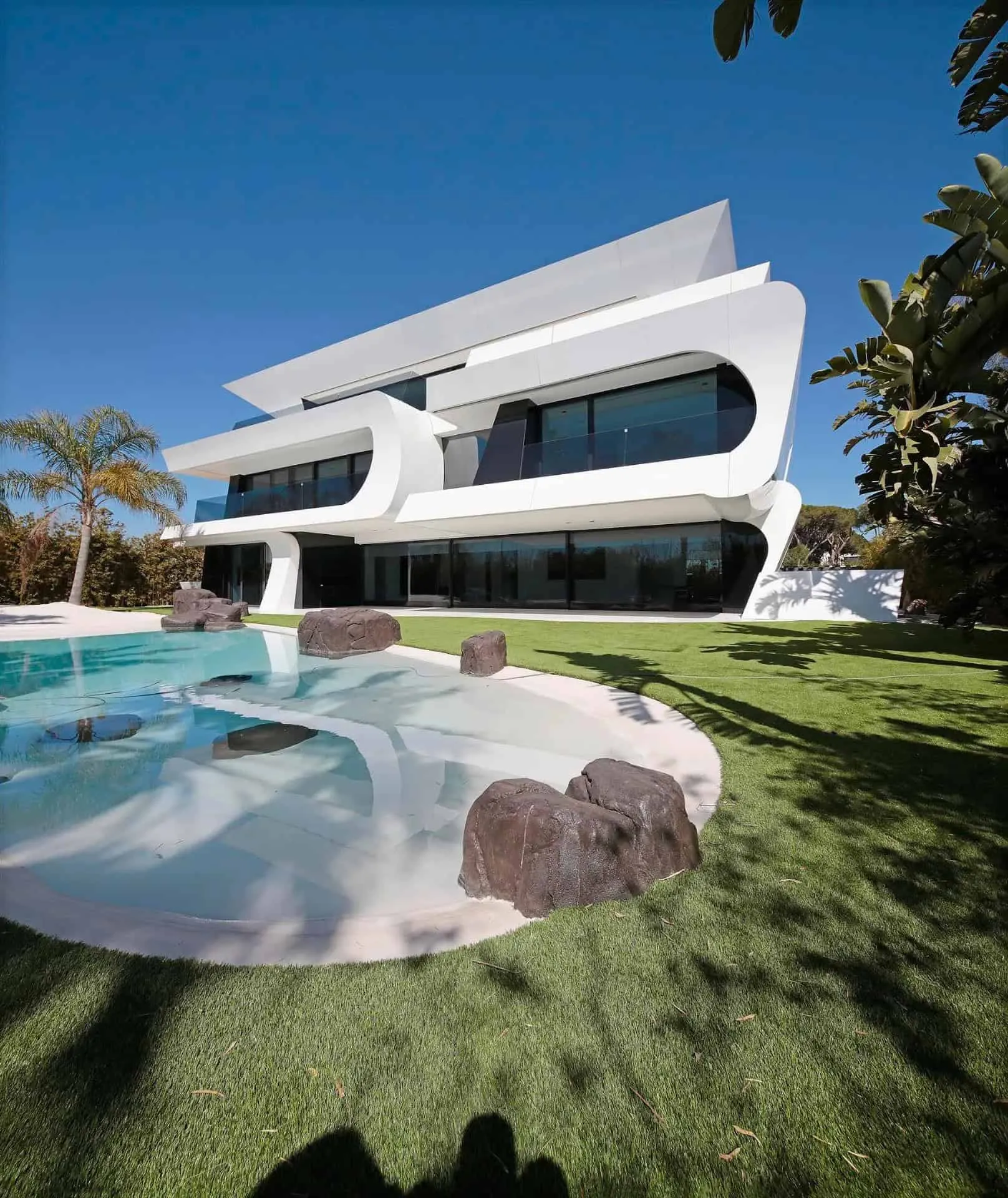 豪华泳池区域，配有棕榈树和弯曲的人工沙滩，靠近现代别墅