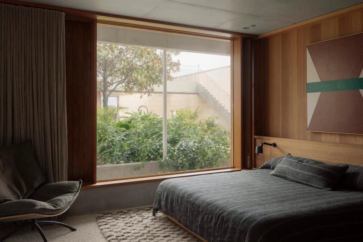 Warm minimalist bedroom with large window overlooking green courtyard in Newcastle