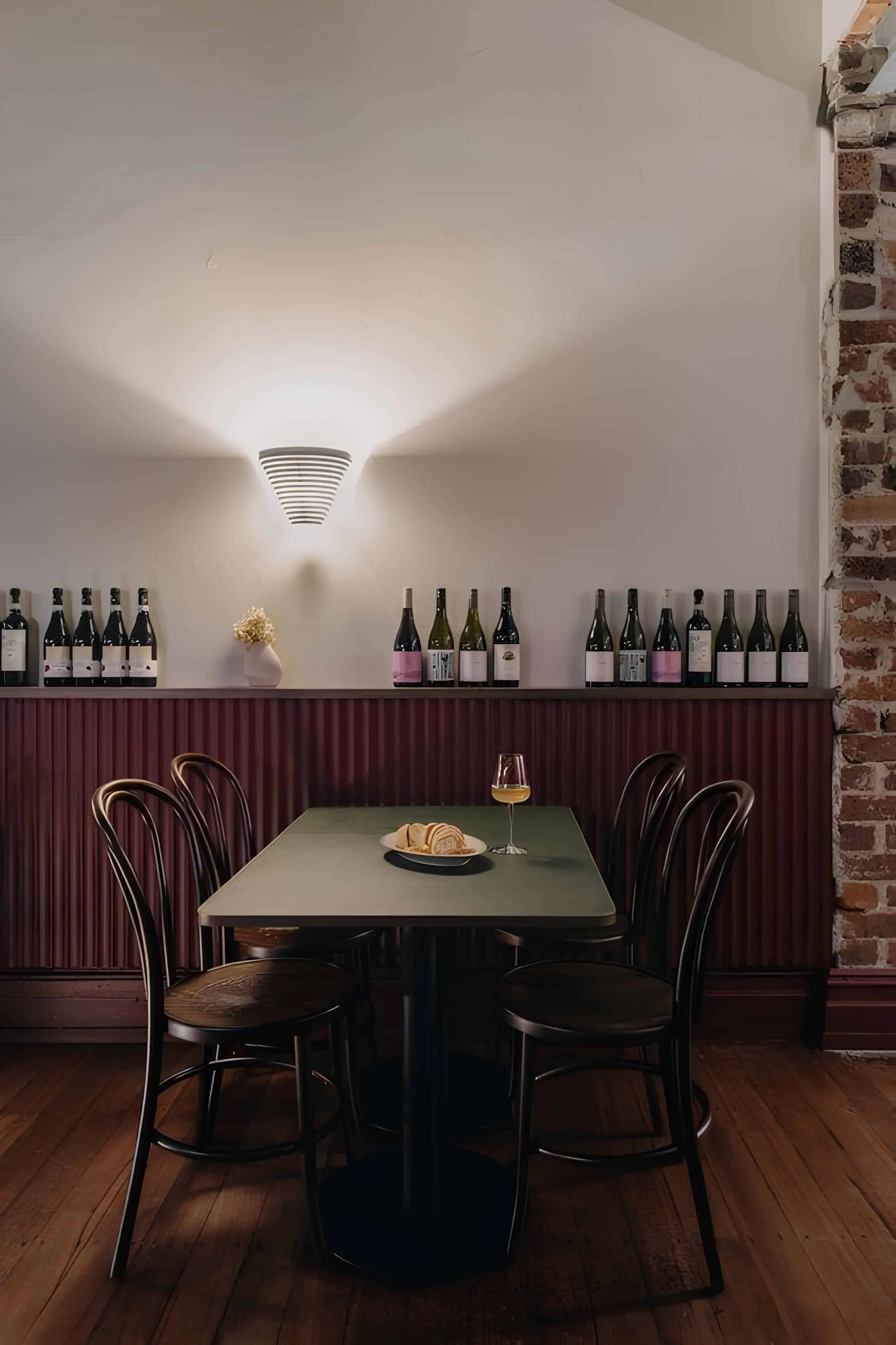 Small dining table with wine and bread, surrounded by bottles of wine and wall lighting