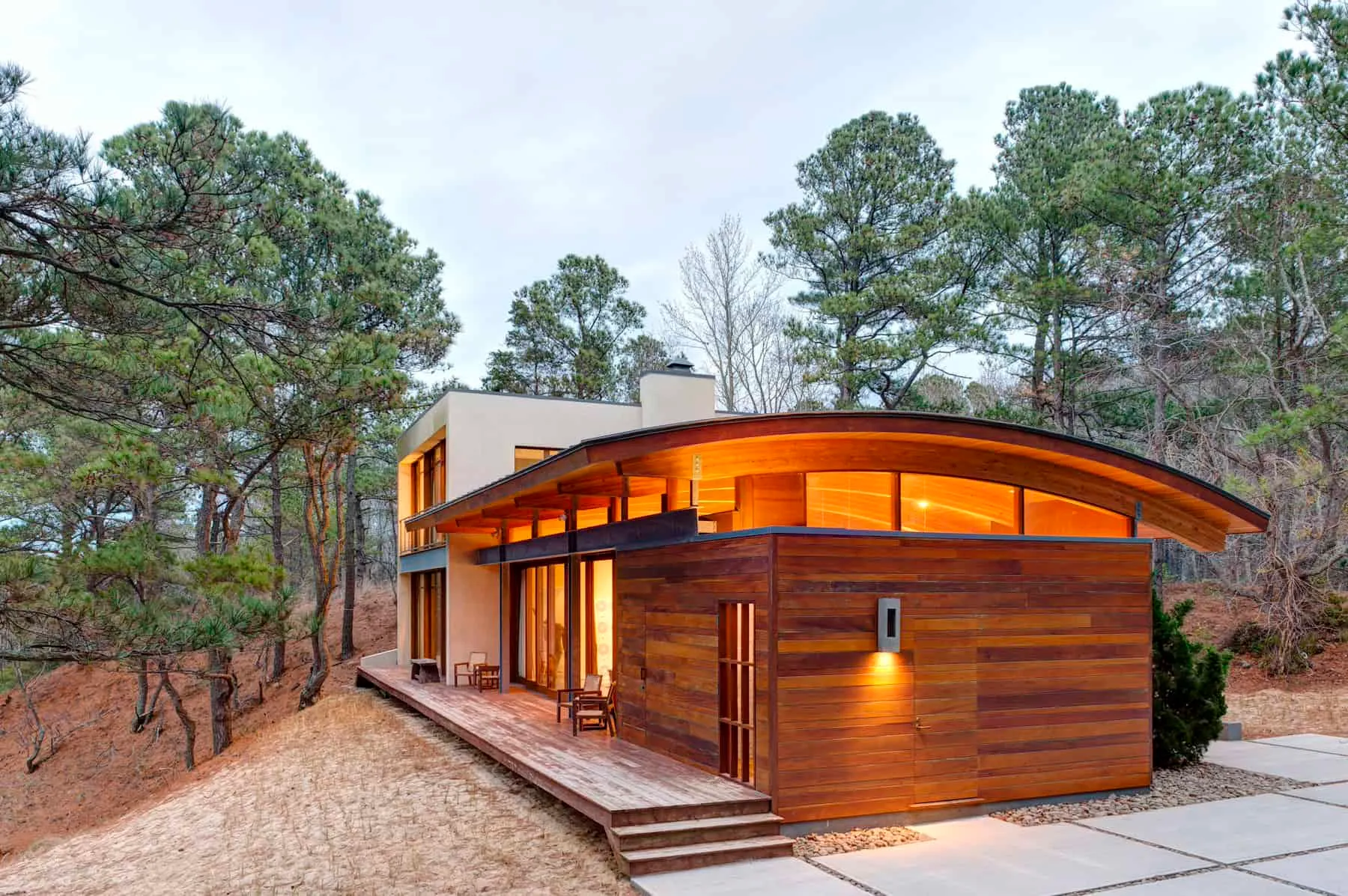 Modern house with an arched roof, wooden cladding and surrounded by forest