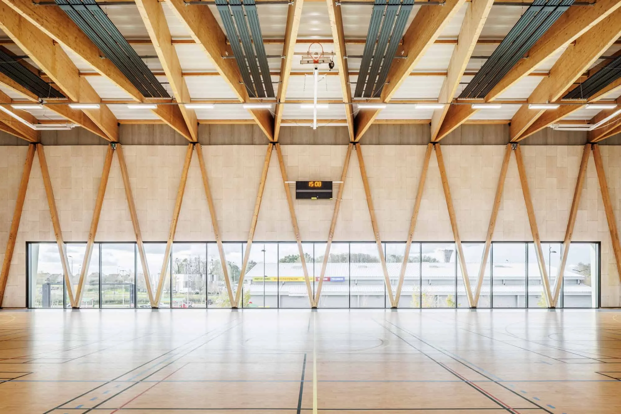 Wooden structure and glass walls creating a bright interior space of the Mennese Sports Complex.